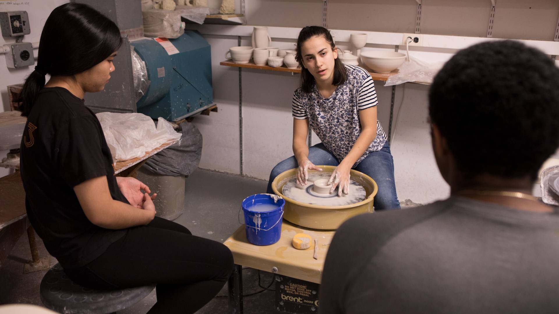 Student demonstrating wheel throwing with clay