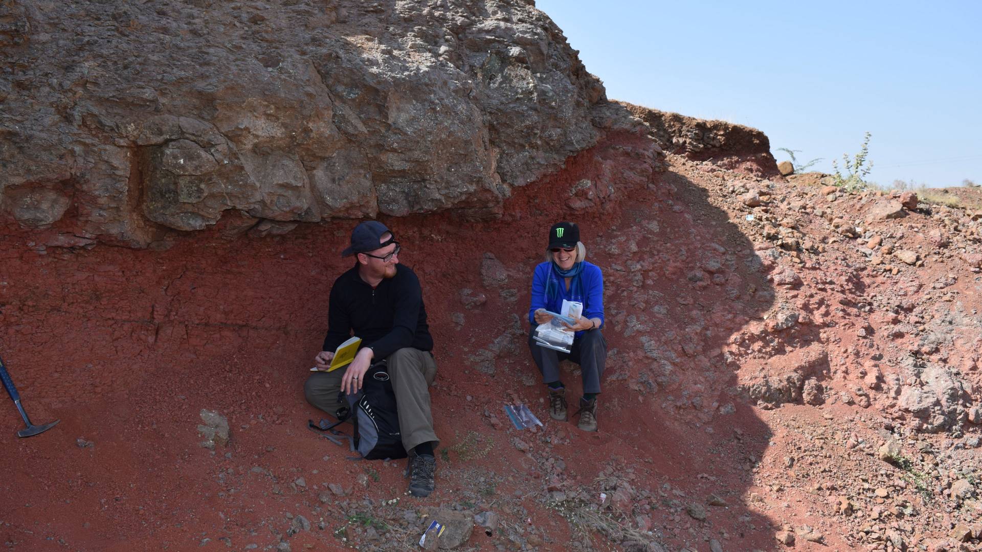 Kyle Samperton and Gerta Keller sitting on ground by lava rock wall