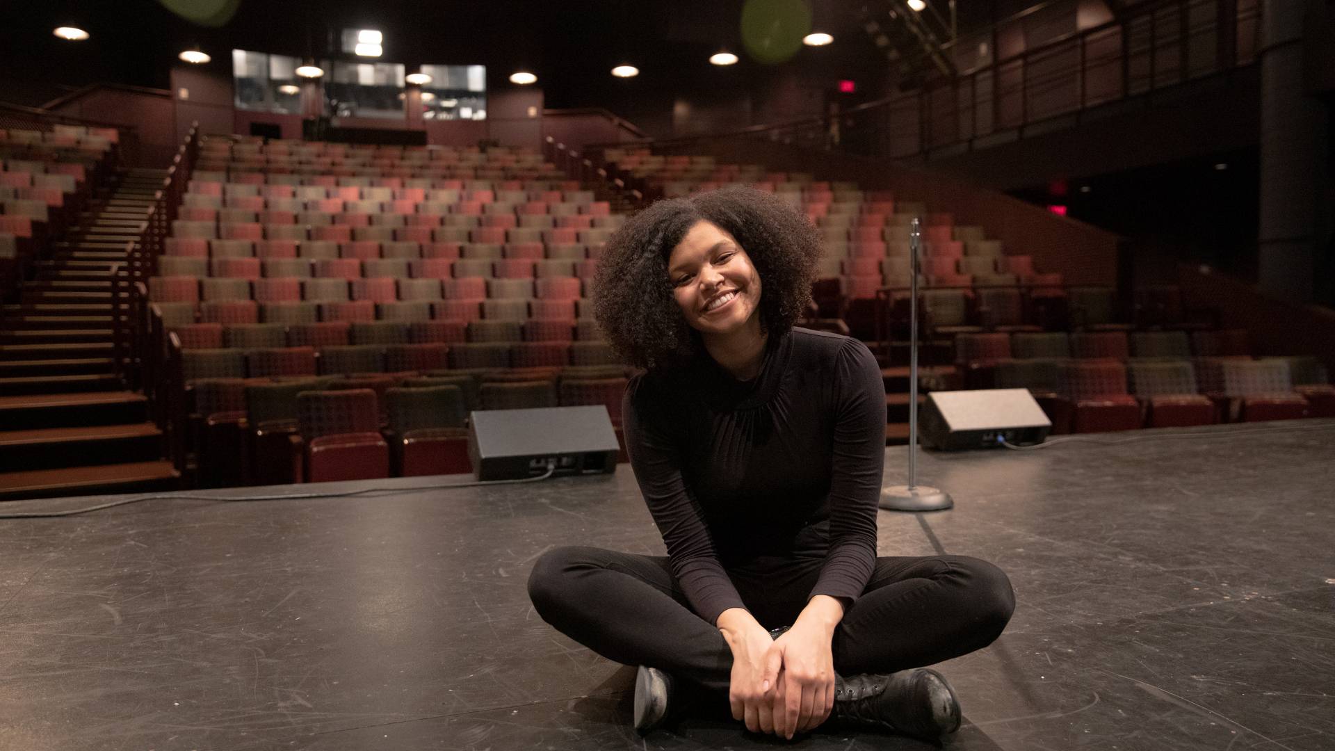 Danielle Davidjohn sitting cross-legged on a stage