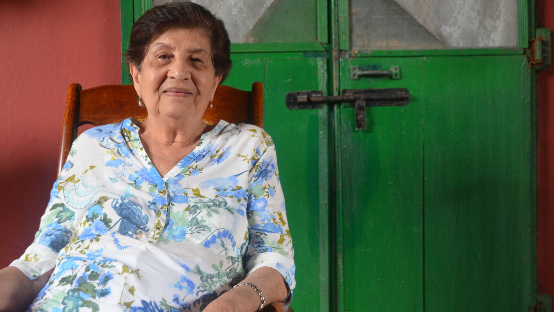 Woman sitting in rocking chair in front of green doors