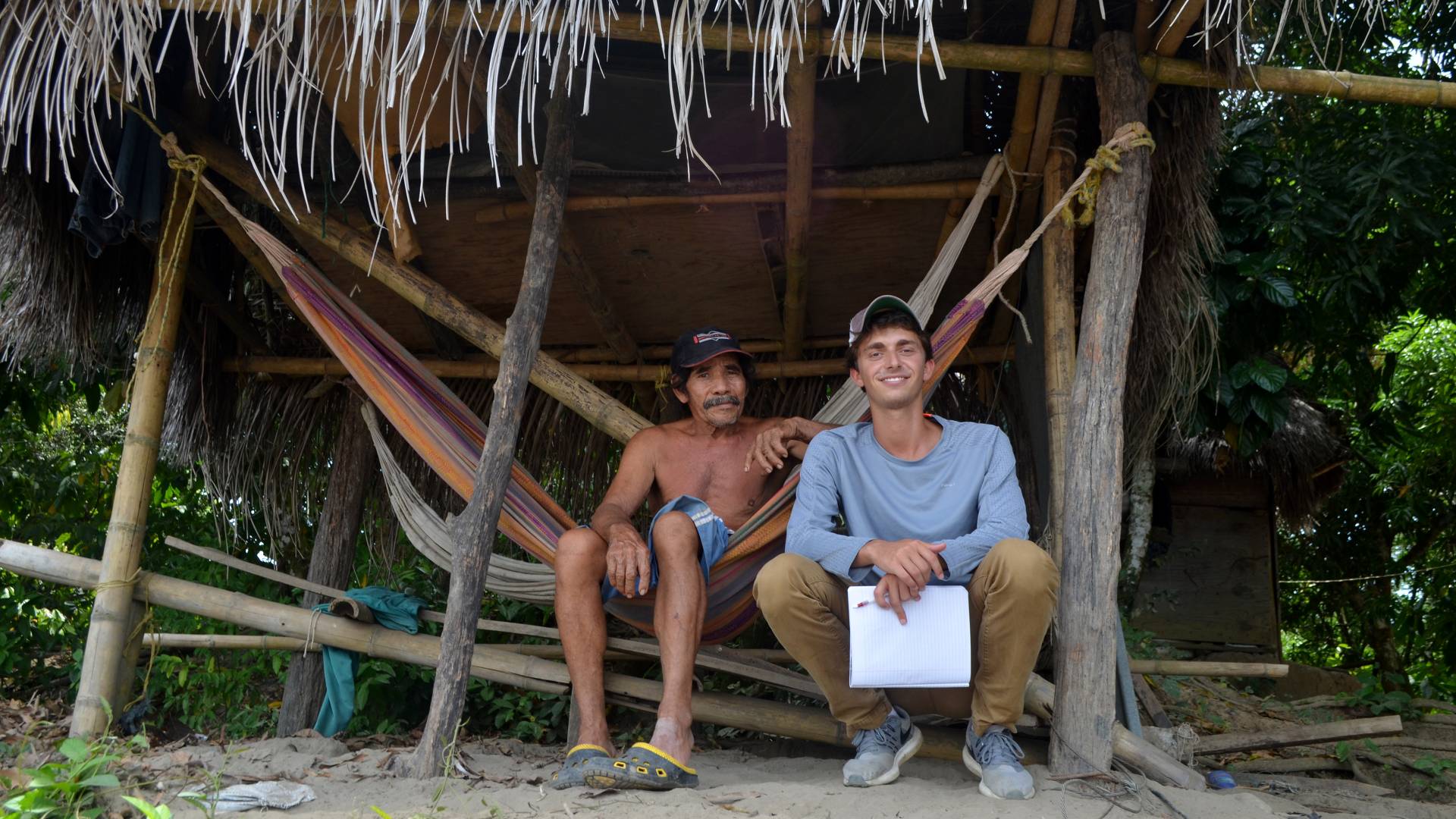 Jordan Salama sitting with elderly man in fishing shack