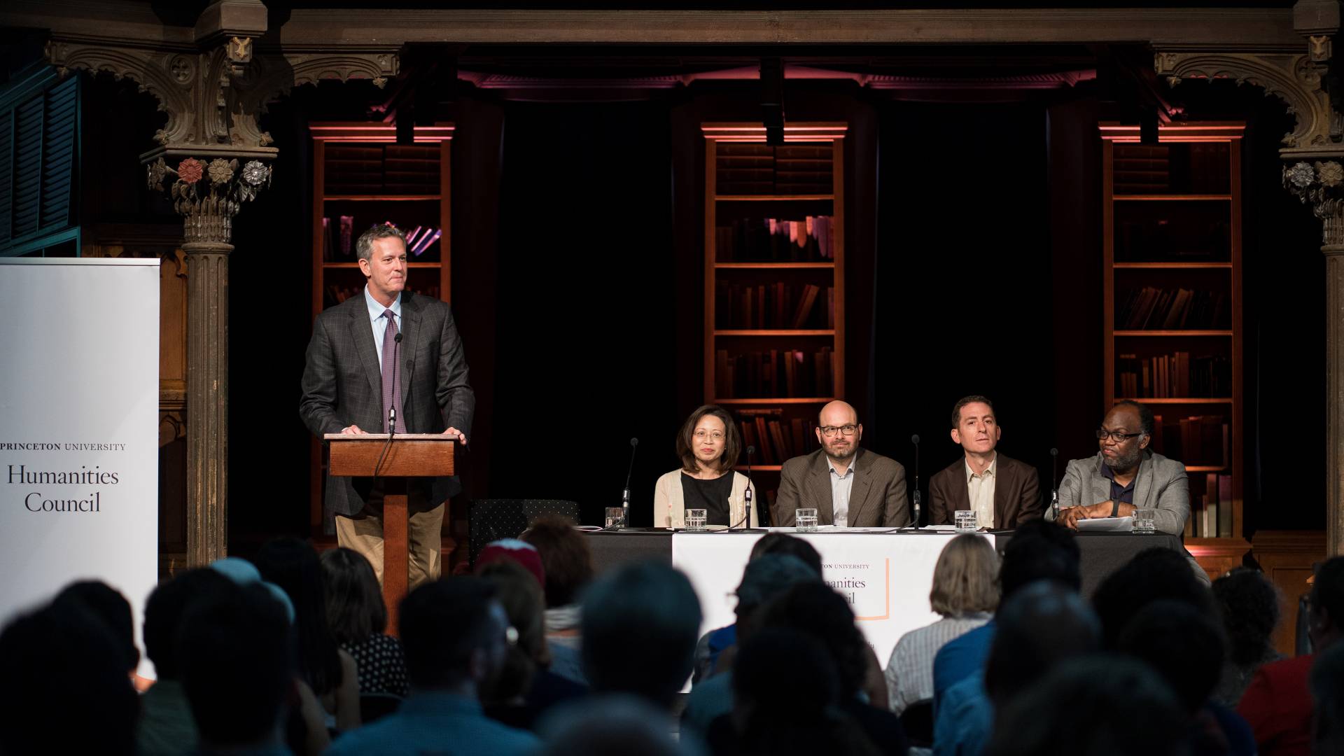 Prof Eric Gregory speaks at the podium with a faculty panel beside him