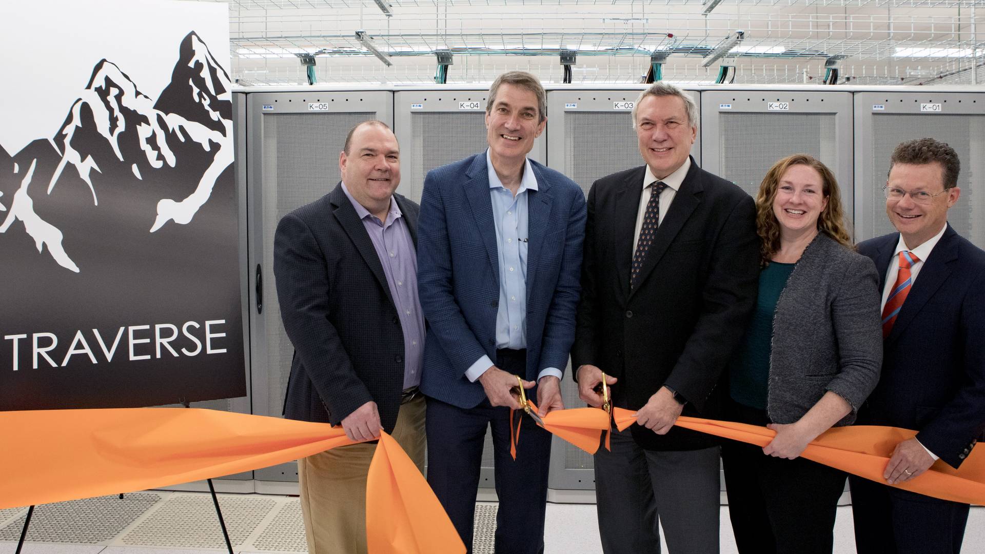5 people cutting an orange ribbon in front of a sign reading "Traverse"