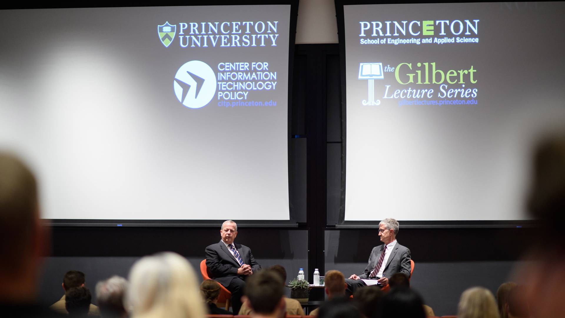 2 men on a stage with projections of Princeton University School of Engineering and Applied Science, CITP, Princeton University, and the Gilbert Lecture Series logos on a screen 