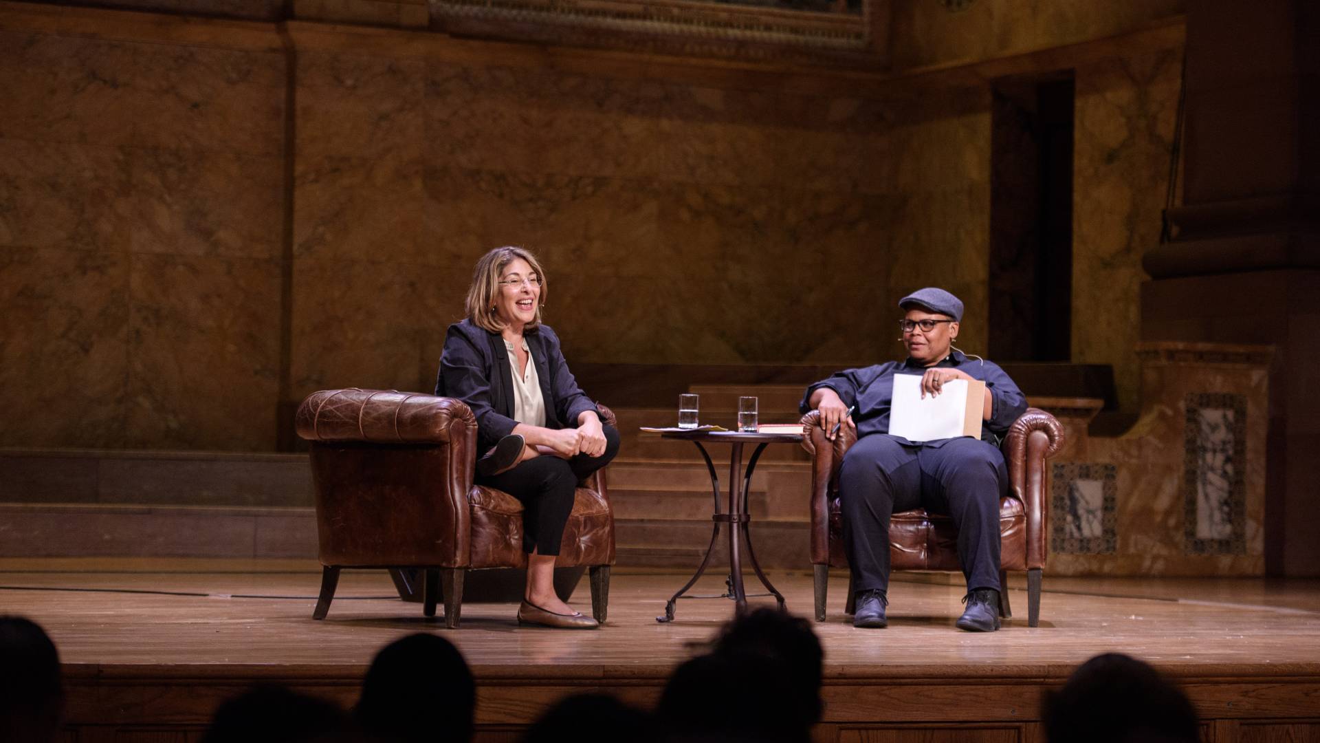 Klein and Taylor, seated in armchairs on stage