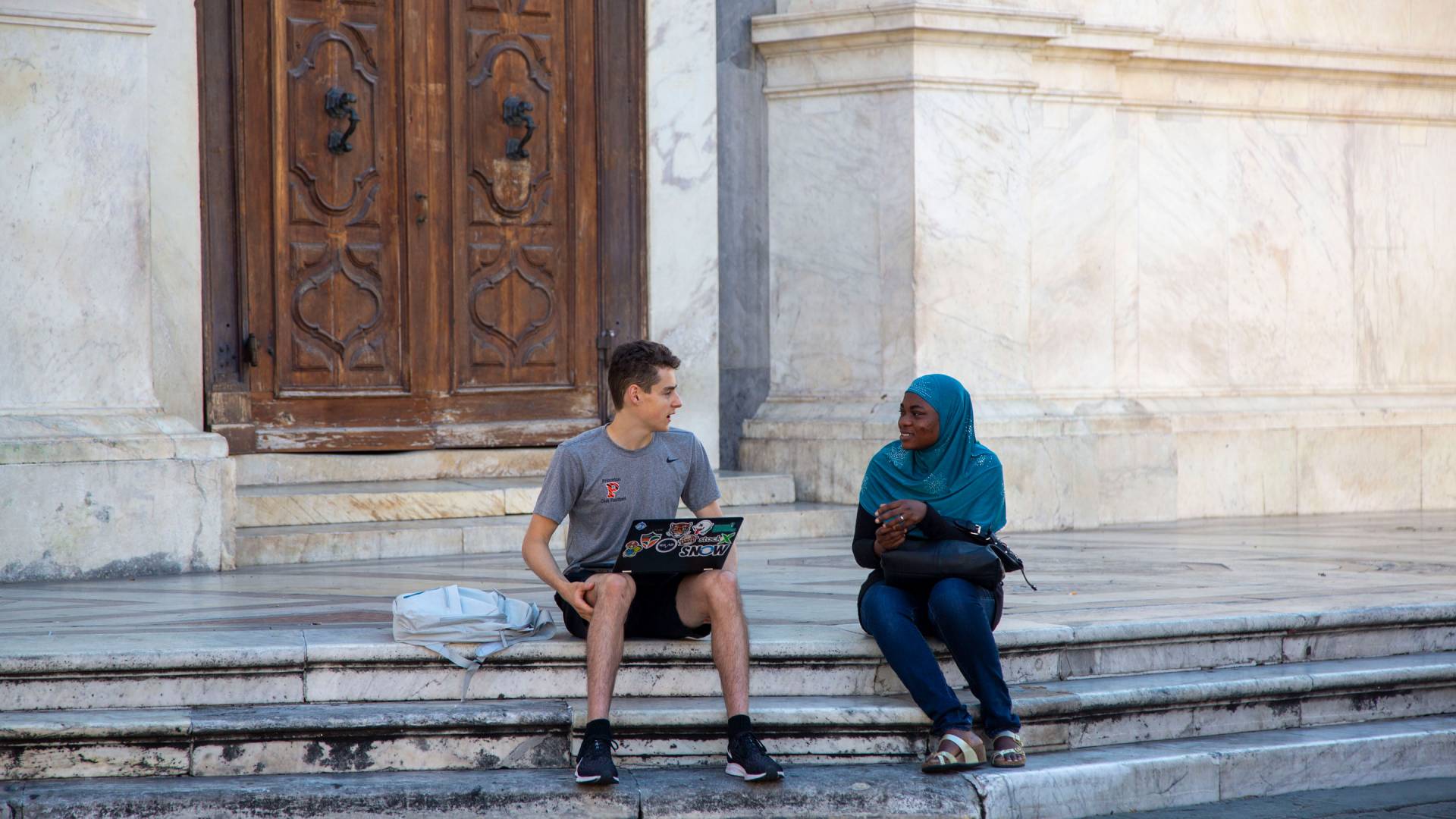 Student interviewing young immigrant sitting on steps