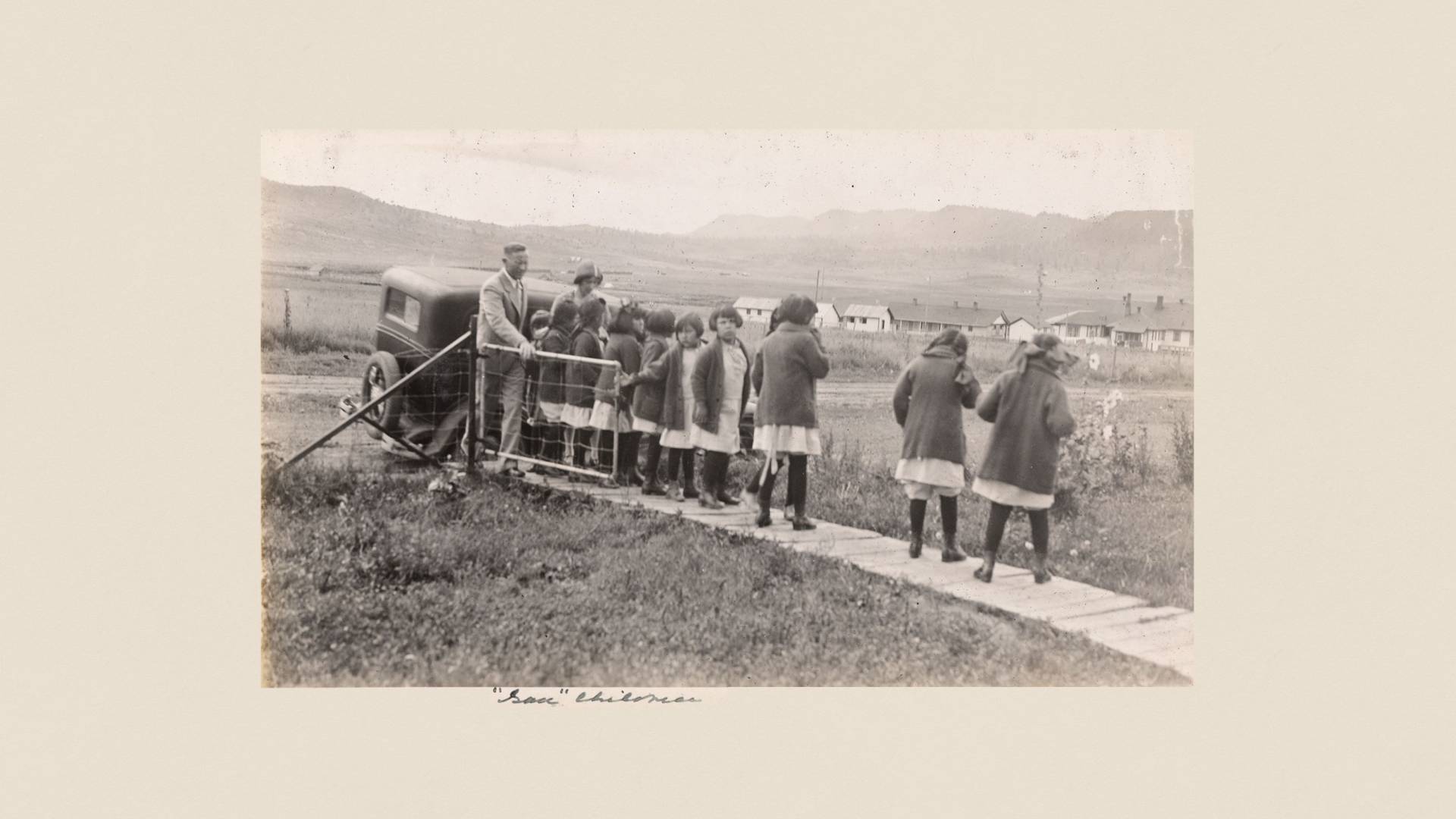 A man with a row of identically dressed girls on a narrow wooden boardwalk