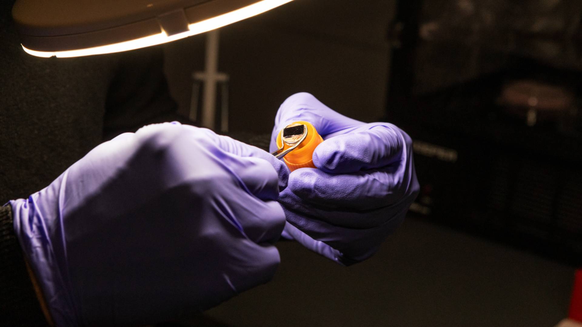 Glove-clad hands hold a tiny rectangular specimen.