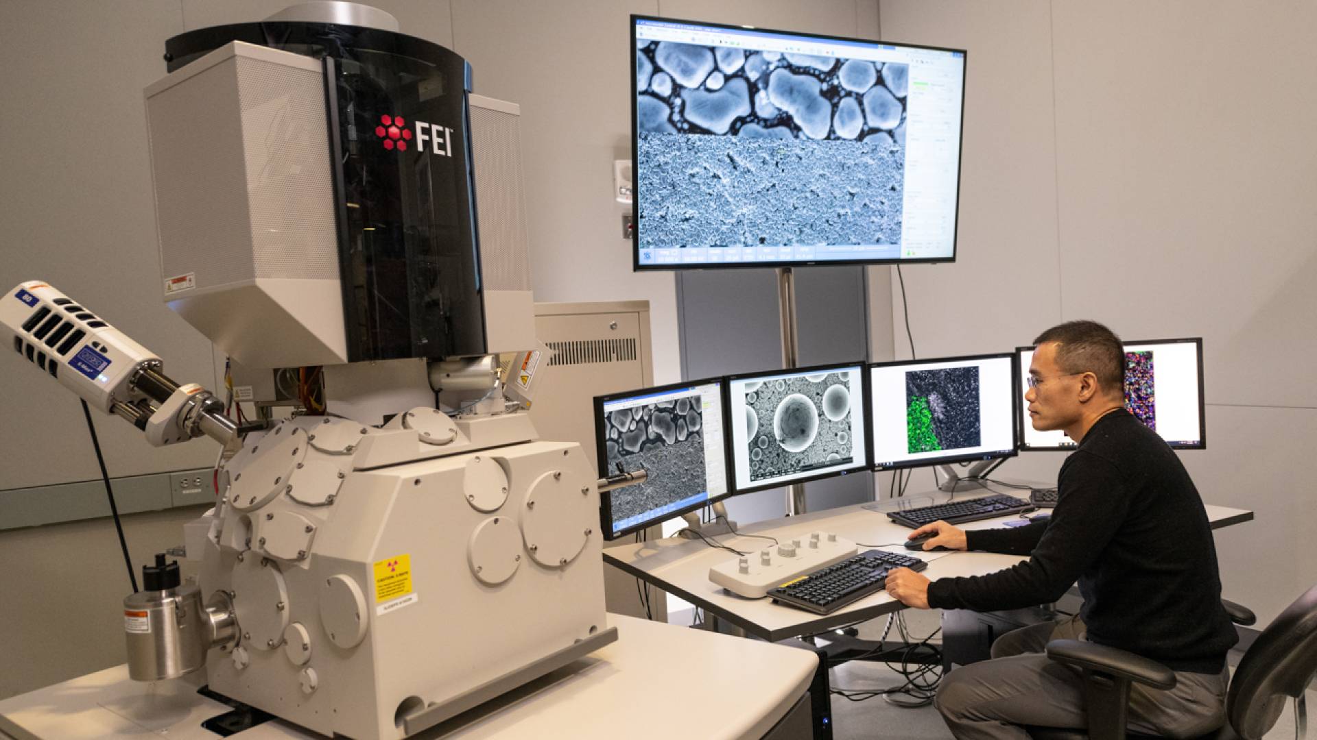 Prof. Yibin Kang sits in front of four screens next to a large machine.