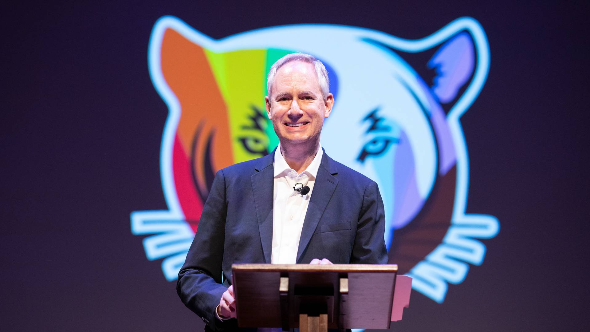 A person on stage with a colorful tiger as background
