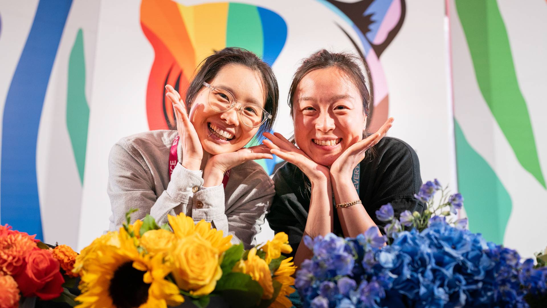 Two individuals smiling with their hands below their chin posing of the camera