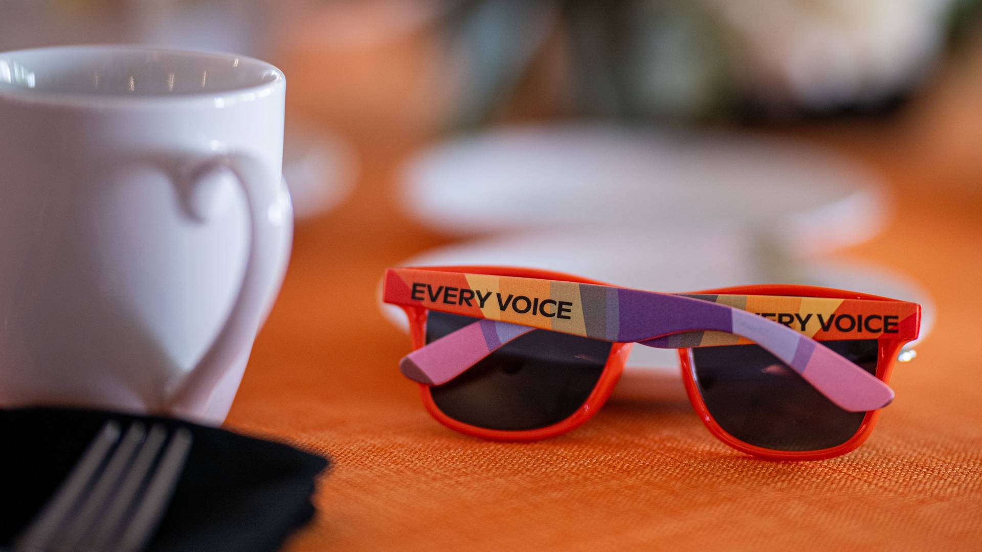 Multi-colored pair of sunglasses next to a cup.