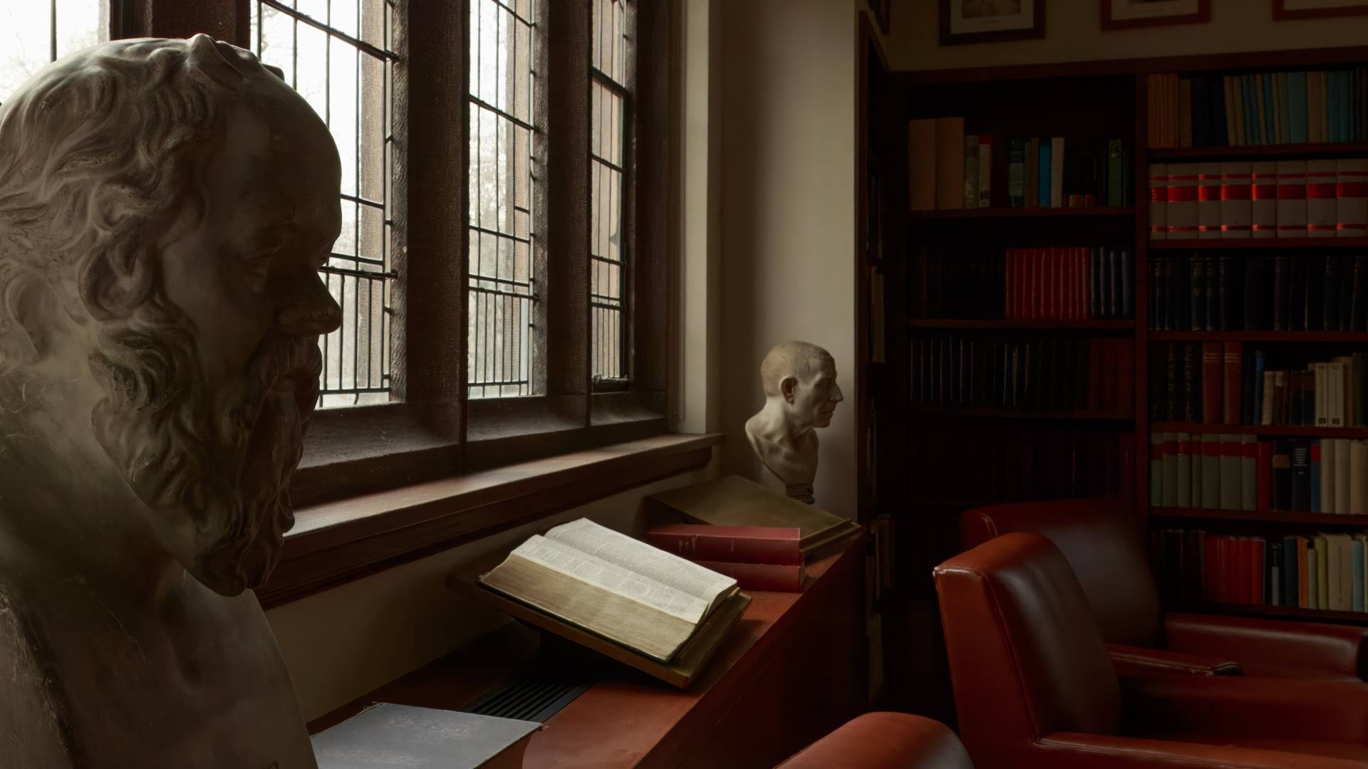 Classical busts flank a large open book on display in a library setting.