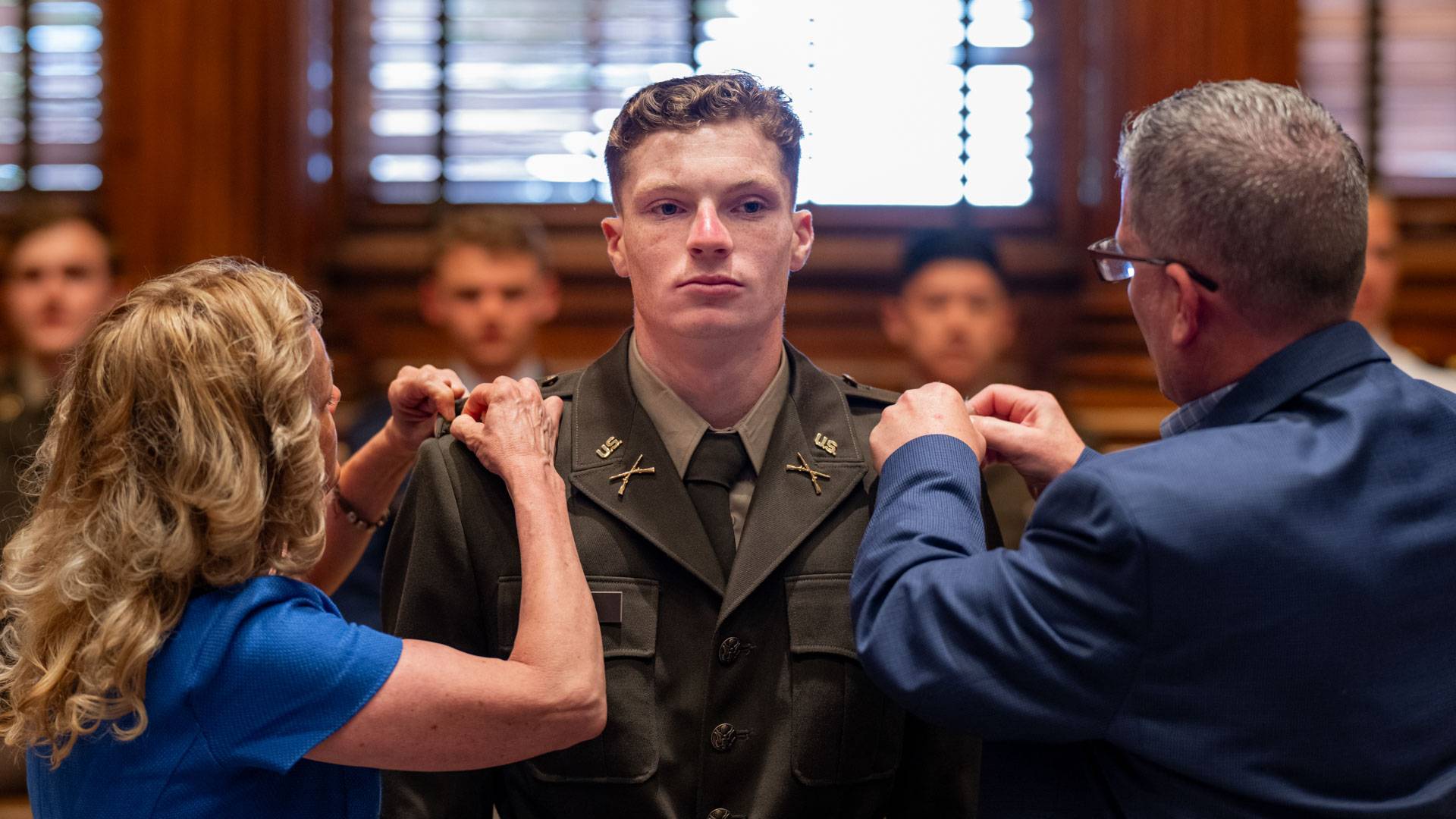 An Army ROTC student is pinned on both sides of his uniform by his mother and father.