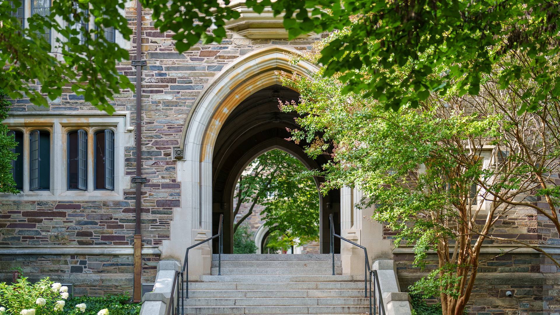Steps leading up to a stone arch that allows pedestrians to walk through a building to the other side.