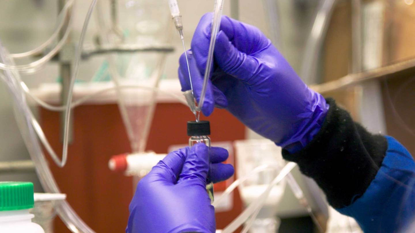 gloved hands hold tubes and a beaker