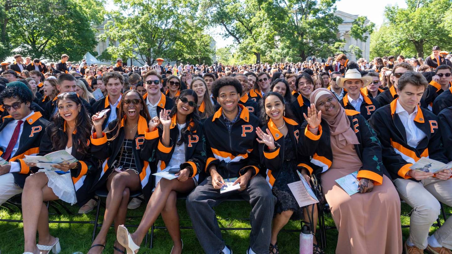 Smiling students in their class jackets seated on Cannon Green