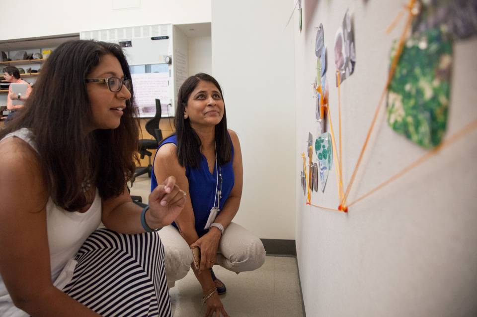 Two QUEST participants look at board with cutouts and thumb tacks