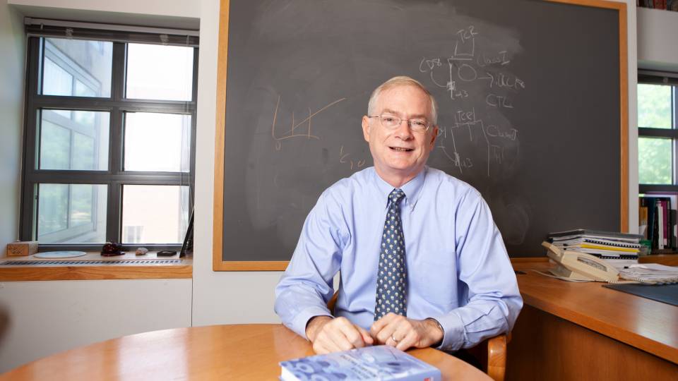 Thomas Shenk sitting at table in front of blackboard