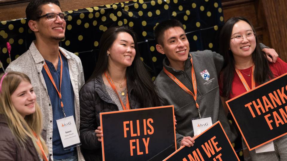 Students standing holding signs that say "FLI IS FLY" and "THANKS FAM"