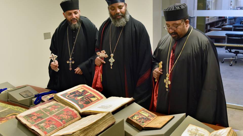 Three visiting priests looking at/discussing a manuscript on a table display