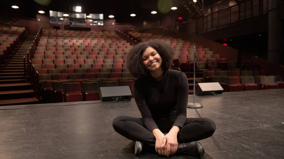 Danielle Davidjohn sitting cross-legged on a stage