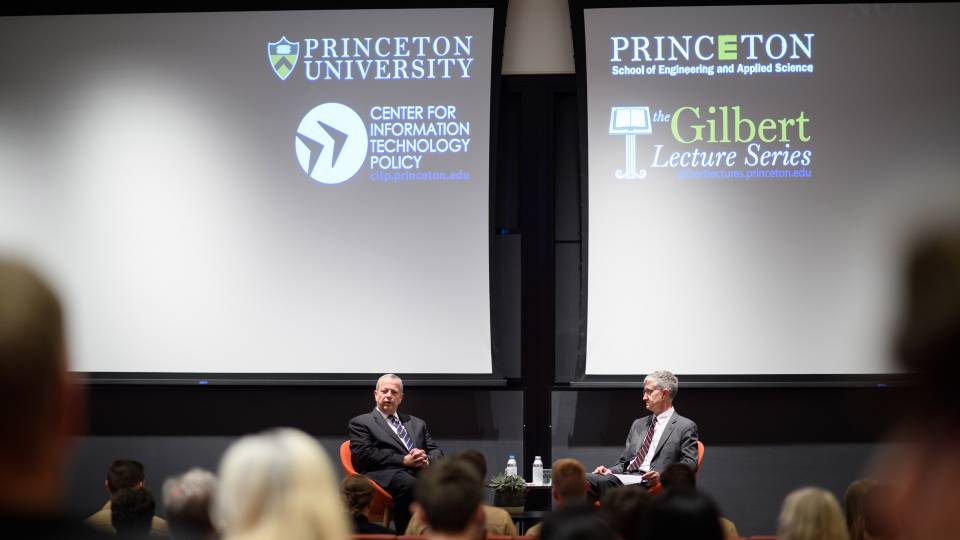 2 men on a stage with projections of Princeton University School of Engineering and Applied Science, CITP, Princeton University, and the Gilbert Lecture Series logos on a screen 