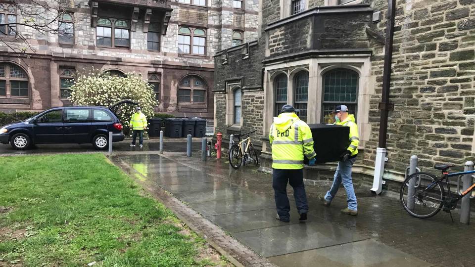 People carry mini refrigerators down a campus walkway