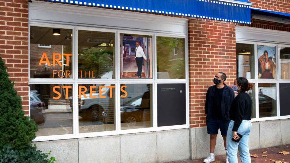 Two pedestrians stop to look at art in shop windows