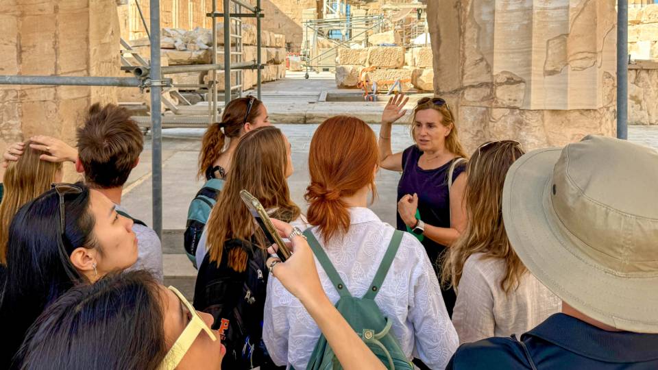 A woman is talking to a group surrounded by ancient pillars.
