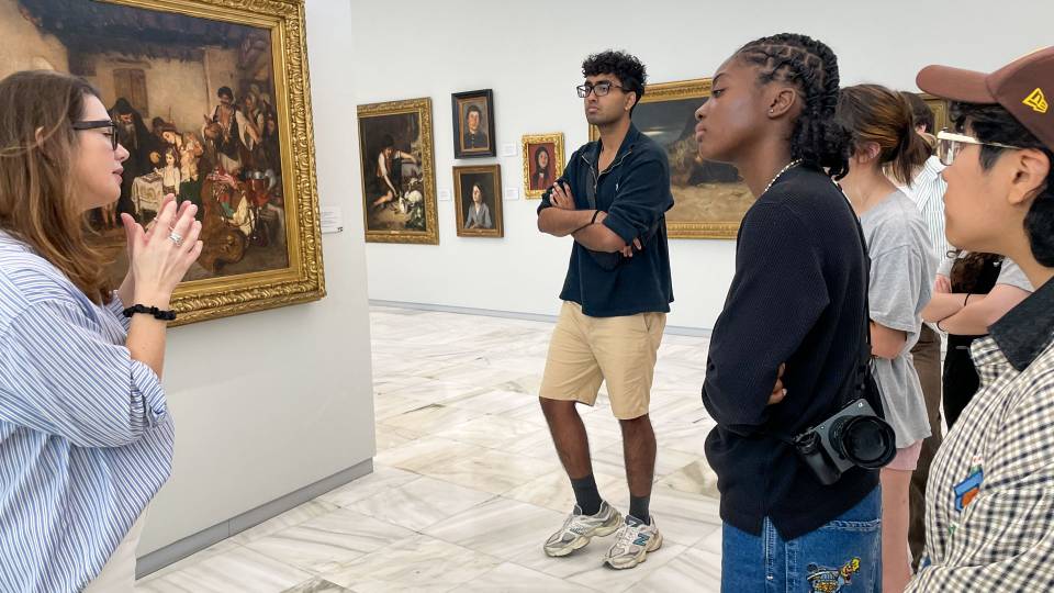 A curator speaks to students about paintings in a museum
