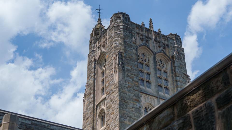 The tower of Firestone Library, with its weather vane visible, stands against the bright blue sky.