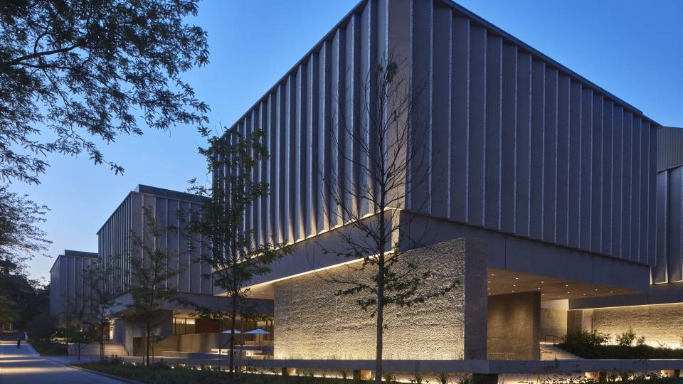 Three fluted concrete exteriors of the new art museum rising into a beautiful deep blue evening sky, that are lit from below