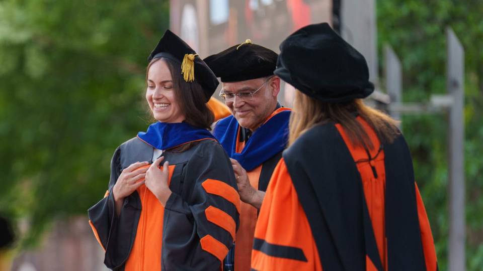 A faculty adviser drapes a graduate student's ceremonial hood 