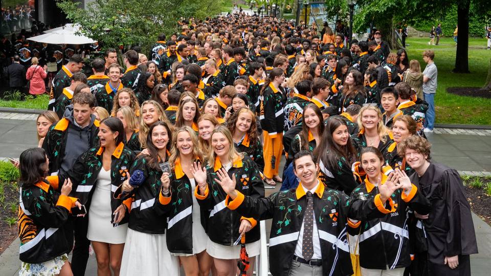 A large number of students wearing their class jackets smiling and waving