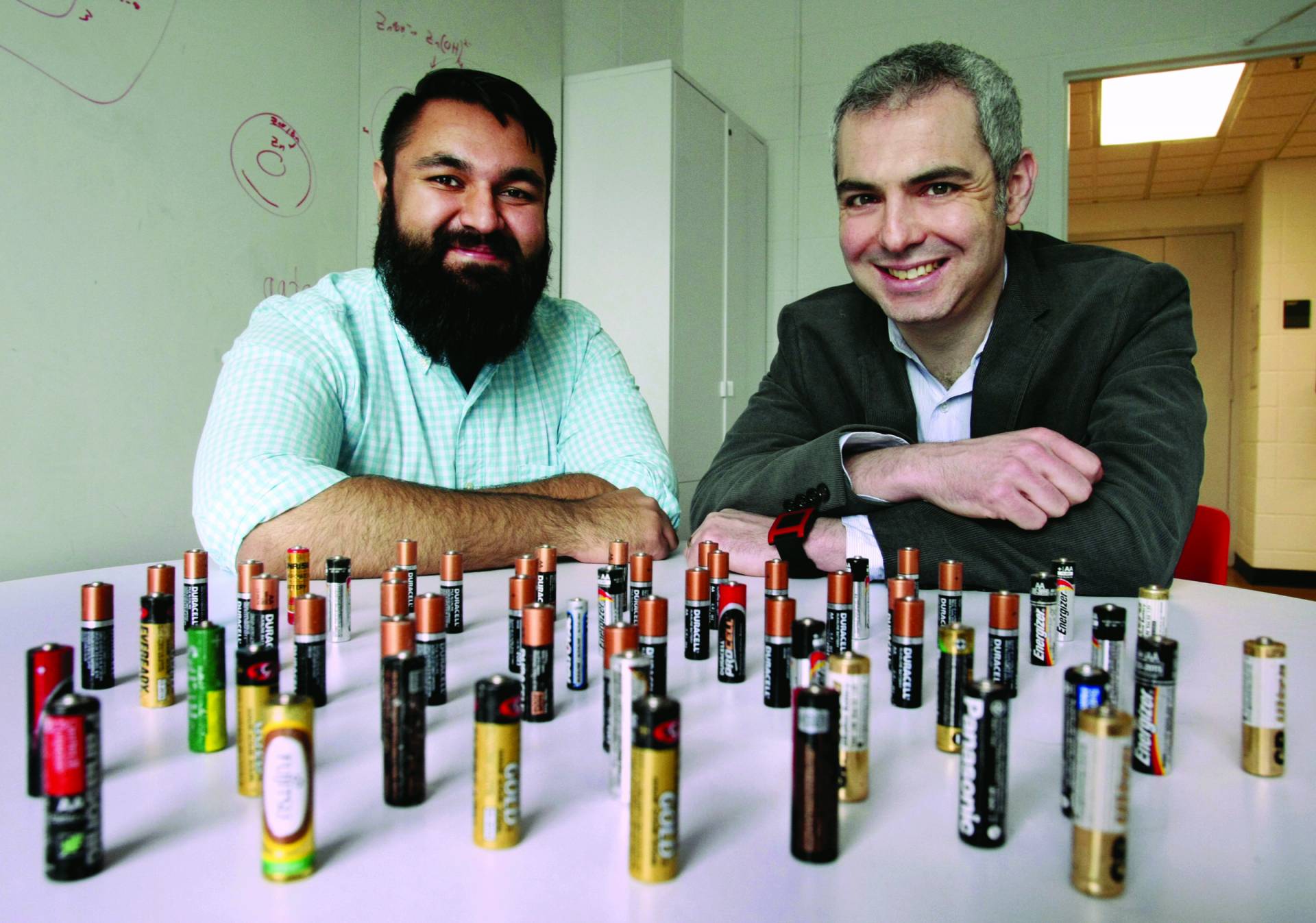 Photo showing two Princeton University researchers sitting at a table on which are displayed AA batteries that they use in their research.