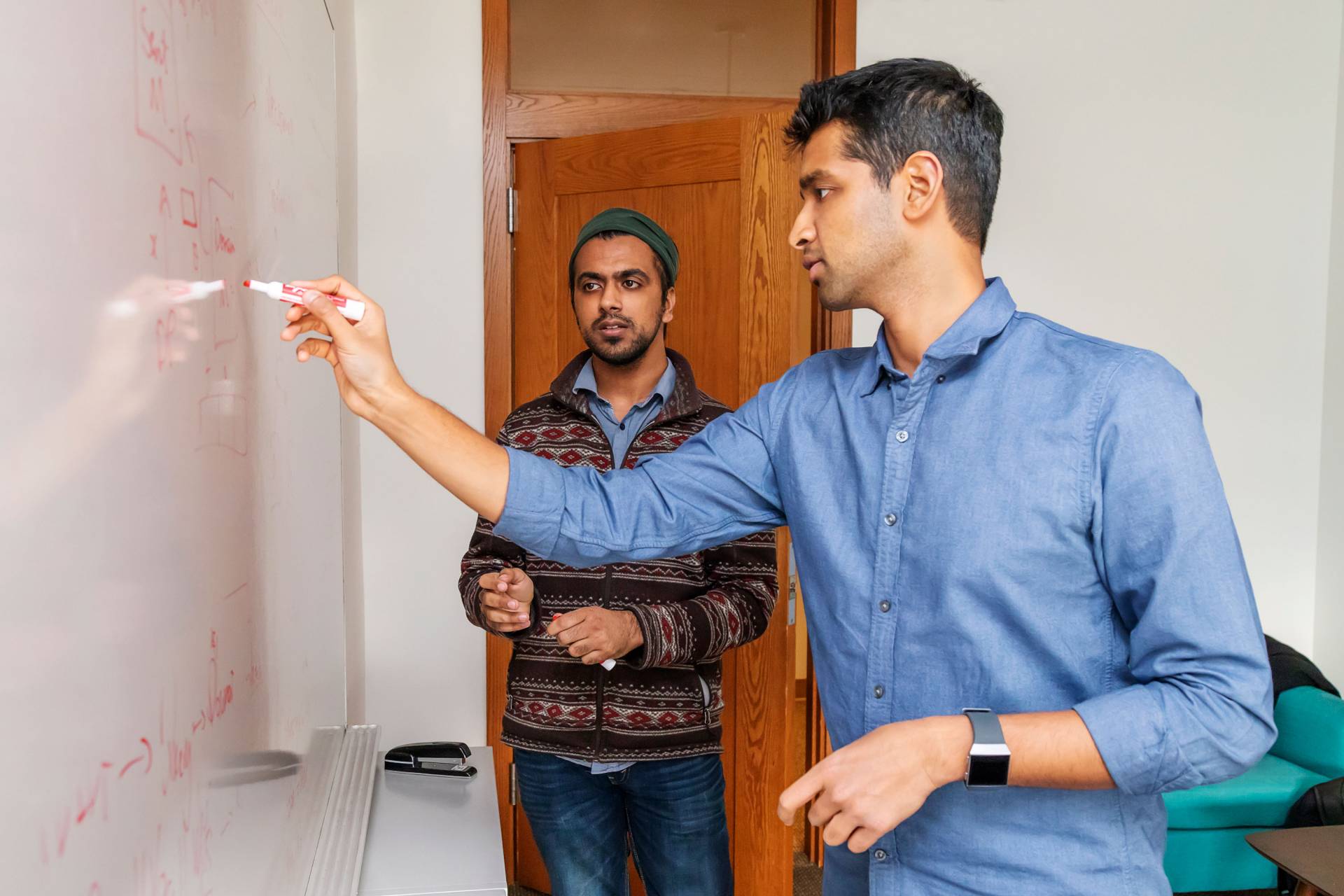 Karthik Narasimhan writes on white board as Karan Arora watches