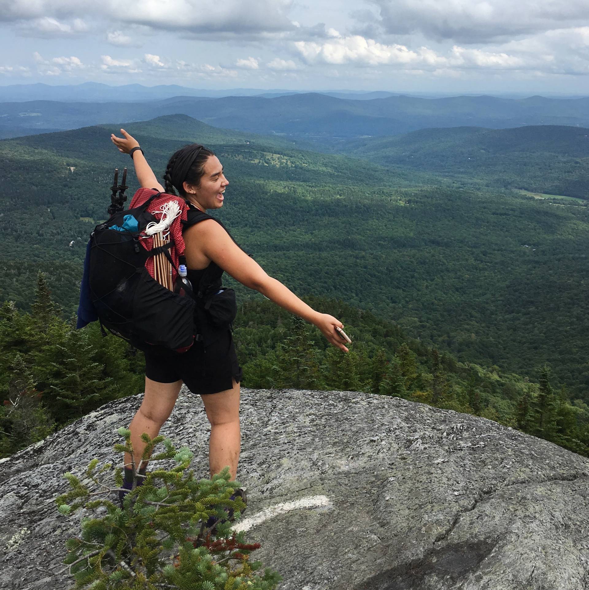 Tess Jacobson stretches out her arms in joy facing a mountainscape
