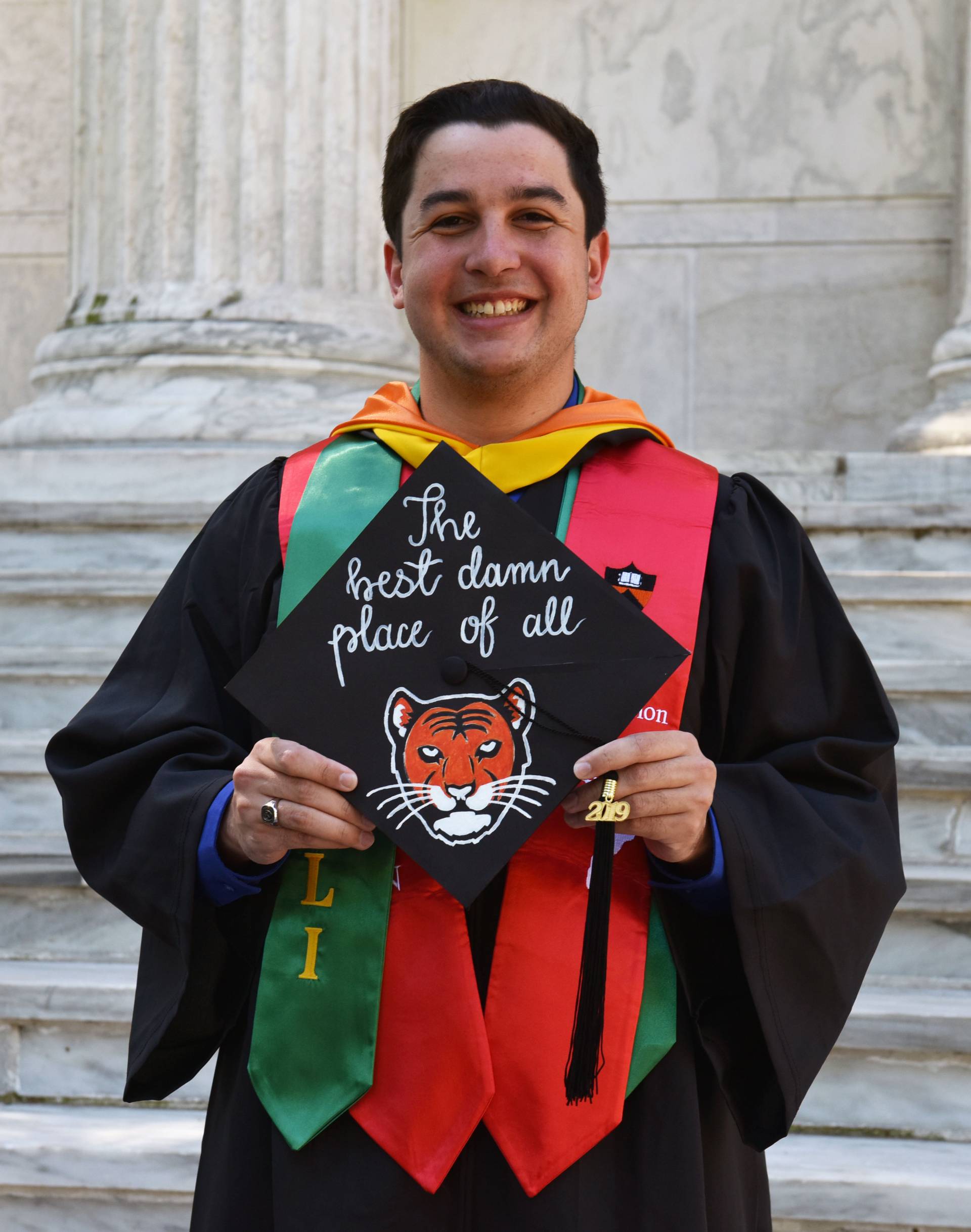 Joseph Puryear III standing with his cap, reading "The best damn place of all"