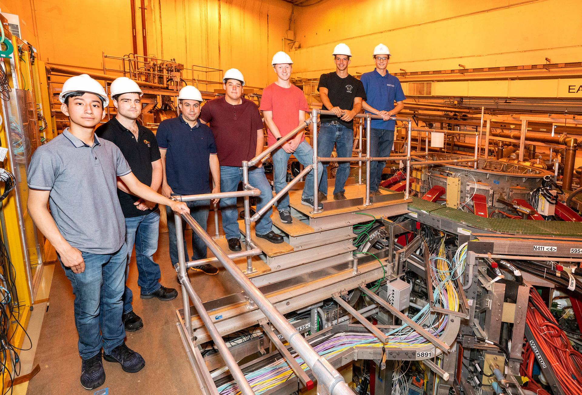 A group of apprentices wearing construction helmets line up 