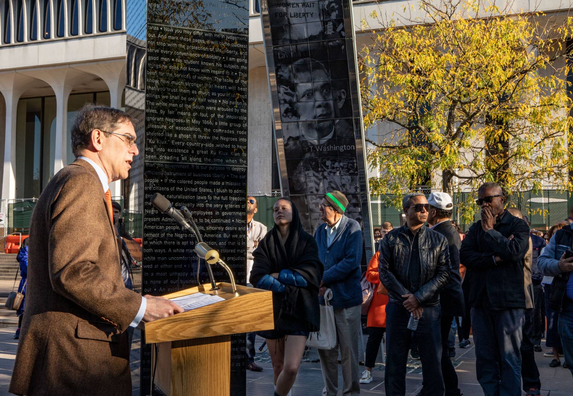 Christopher Eisgrube speaking at podium next to installation