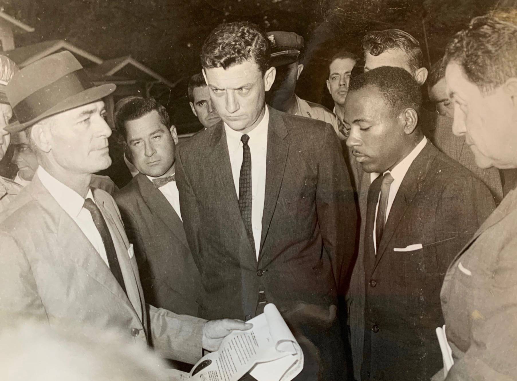 John Doer accompanies John Meredith through a crowd of demonstrators