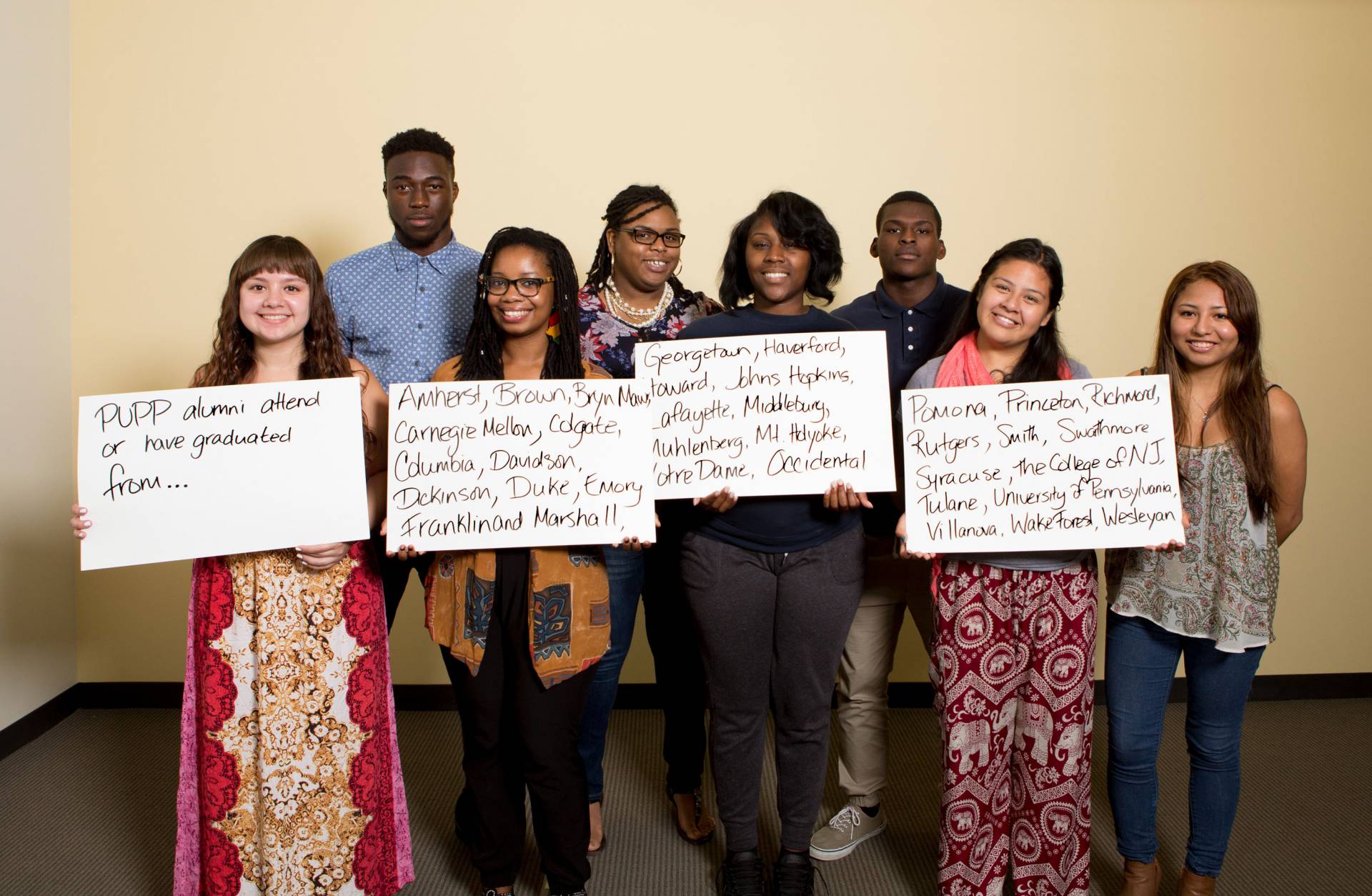 Students holding signs which read, "PUPP alumni have graduated from..." "Amherst, Brown, Carnegie Mellon, Colgate, Columbia, Davidson, Dickinson, Duke, Emory, Franklin and Marshall, Georgetown, Haverford, Howard, Johns Hopkins, Lafayette, Middlebury, Muhlenberg, Mt. Holyoke, Notre Dame, Occidental, Pomona, Princeton, Richmond, Rutgers, Smith, Swarthmore, Syracuse, the College of NJ, Tulane, U of Pennsylvania, Villanova, Wakeforest, Wesleyan"
