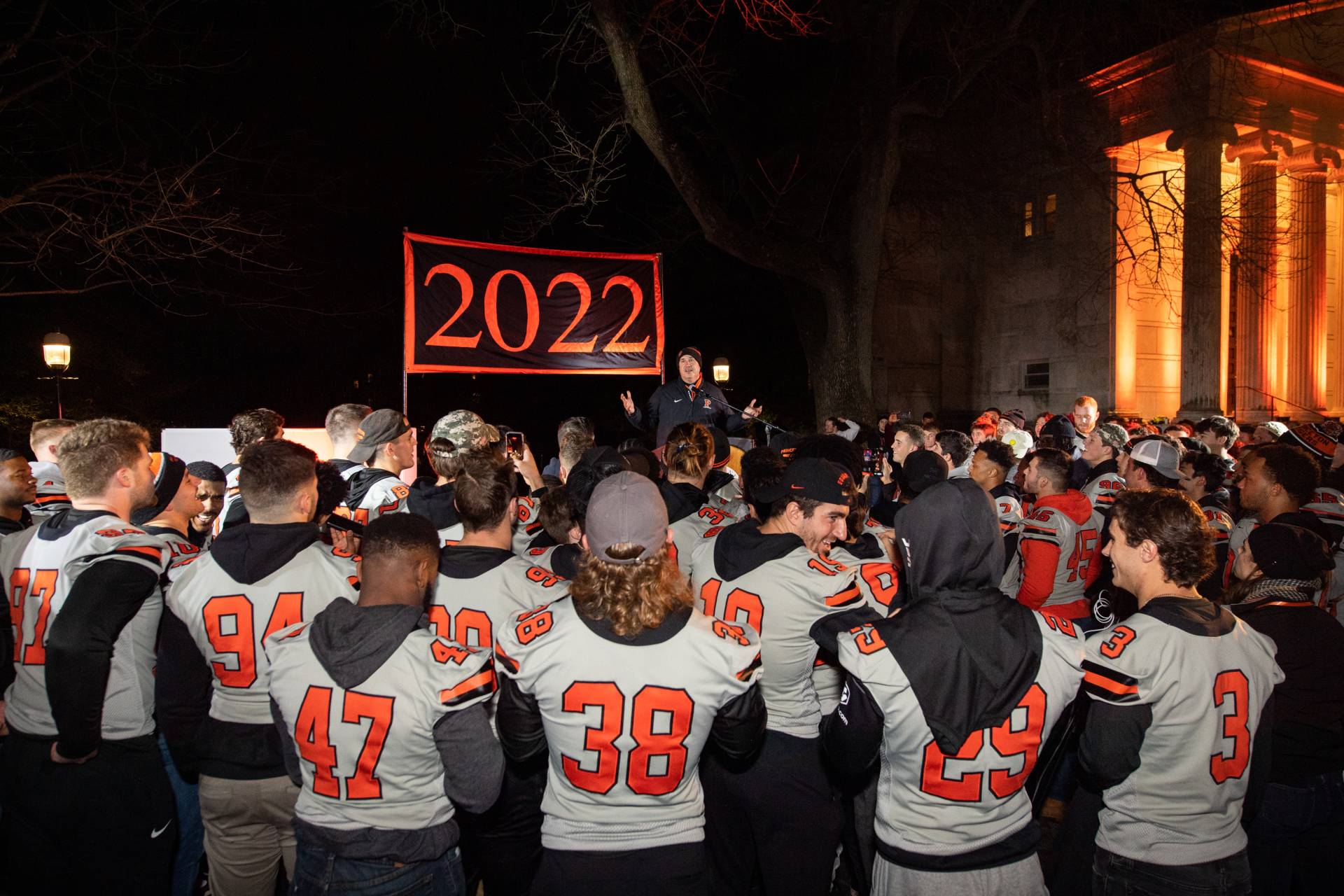 A speaker addresses the football team under a "2022" banner