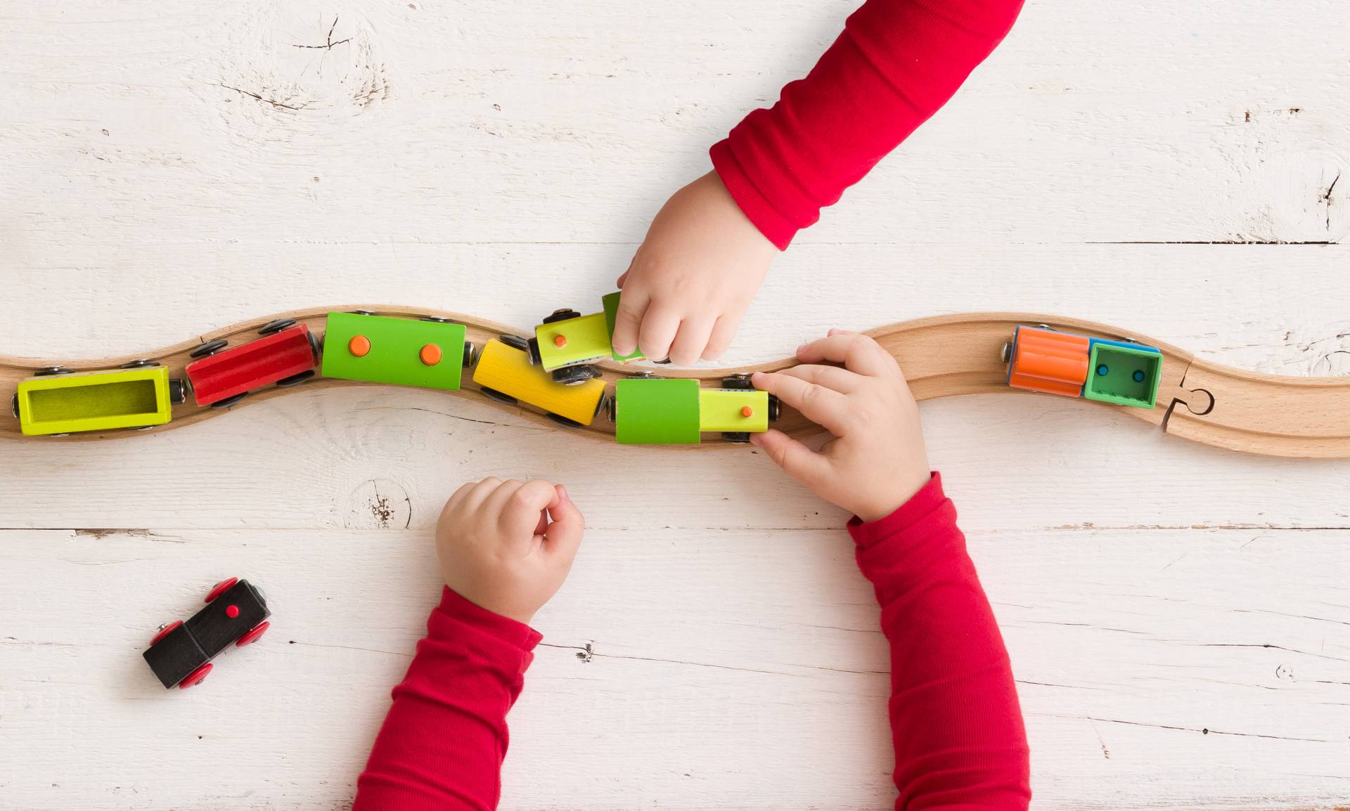 children's hands playing with toy trains