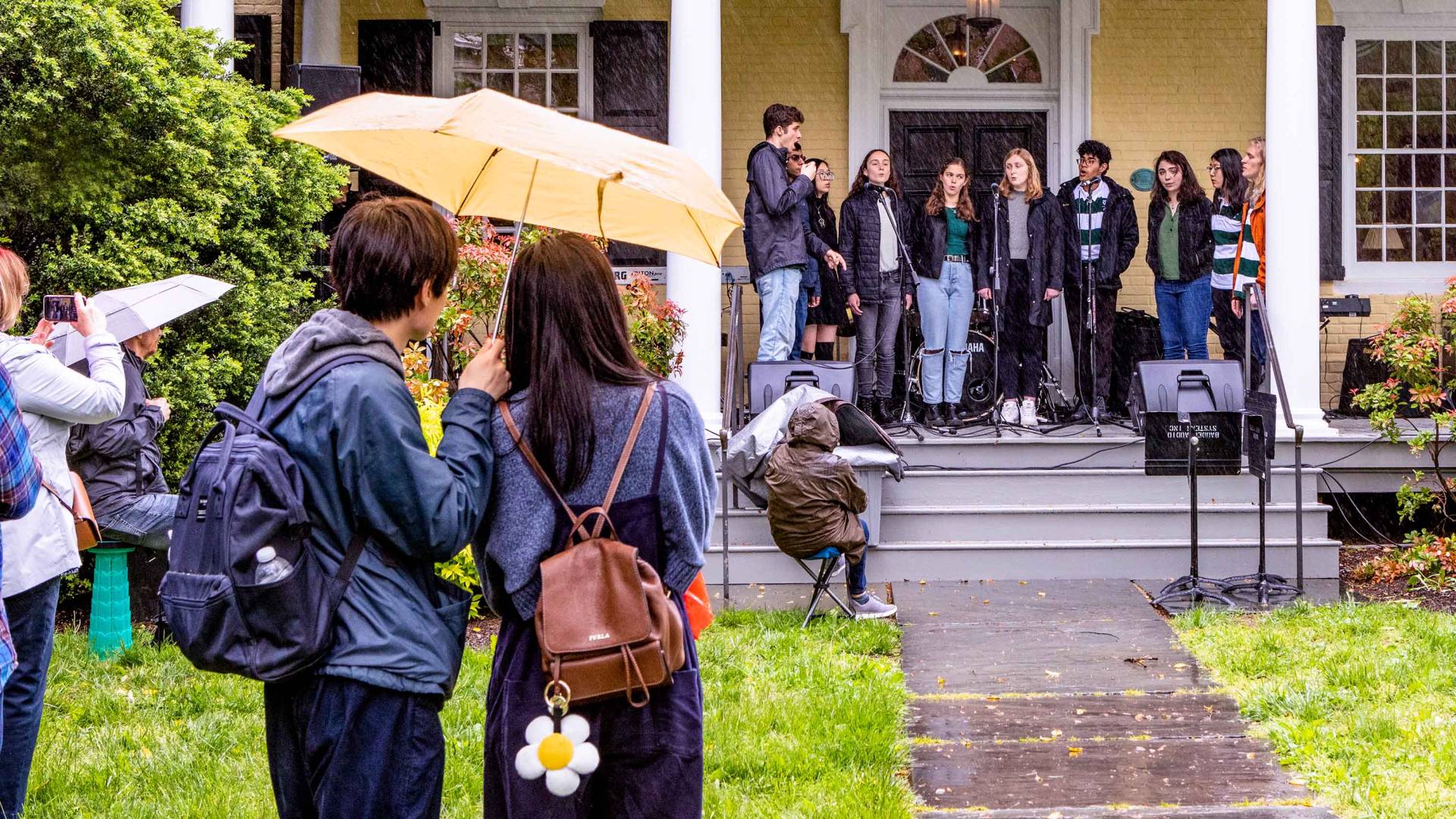 Group singing on a porch while raining.