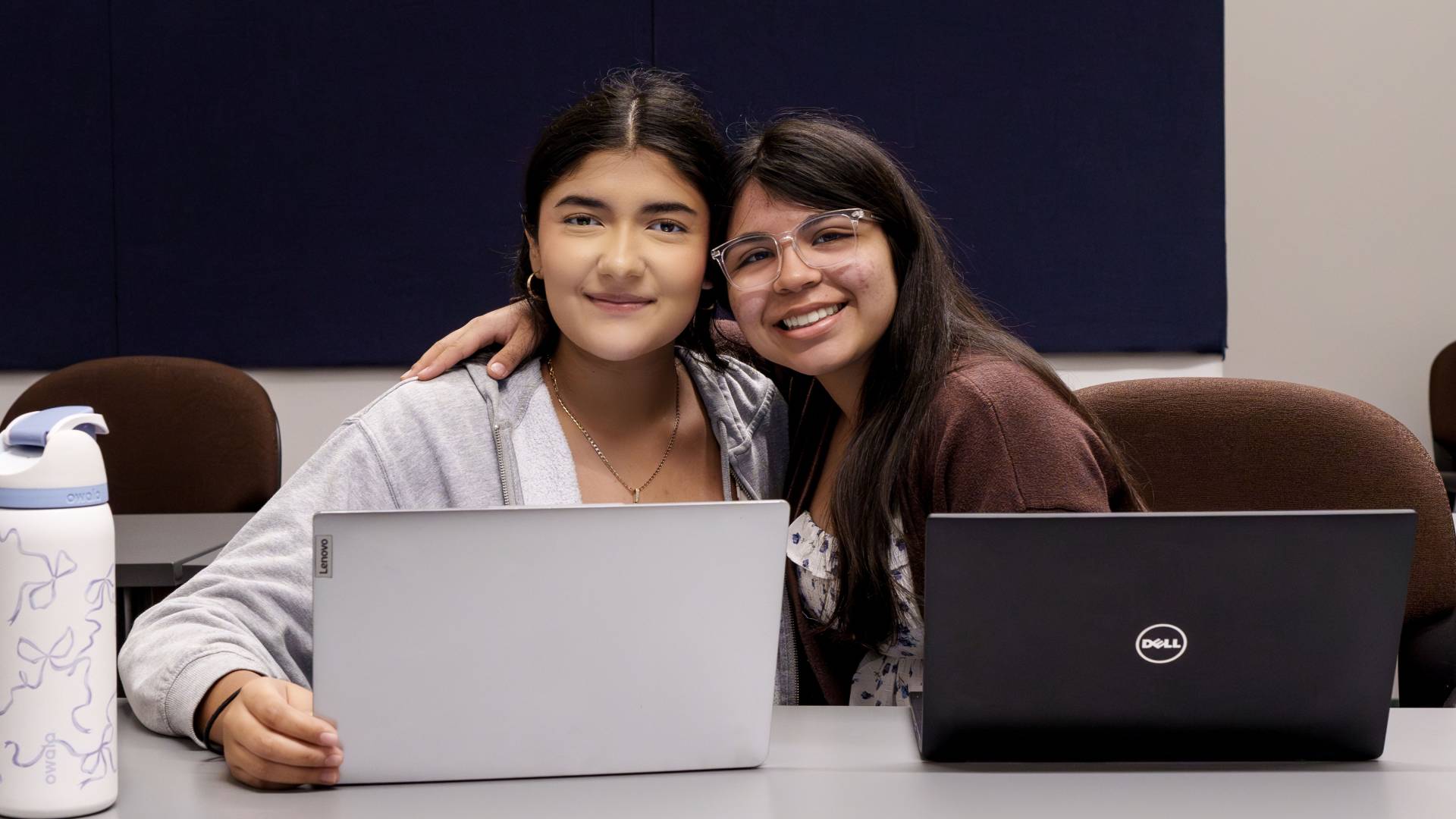 Two students pose for a photo behind their laptops