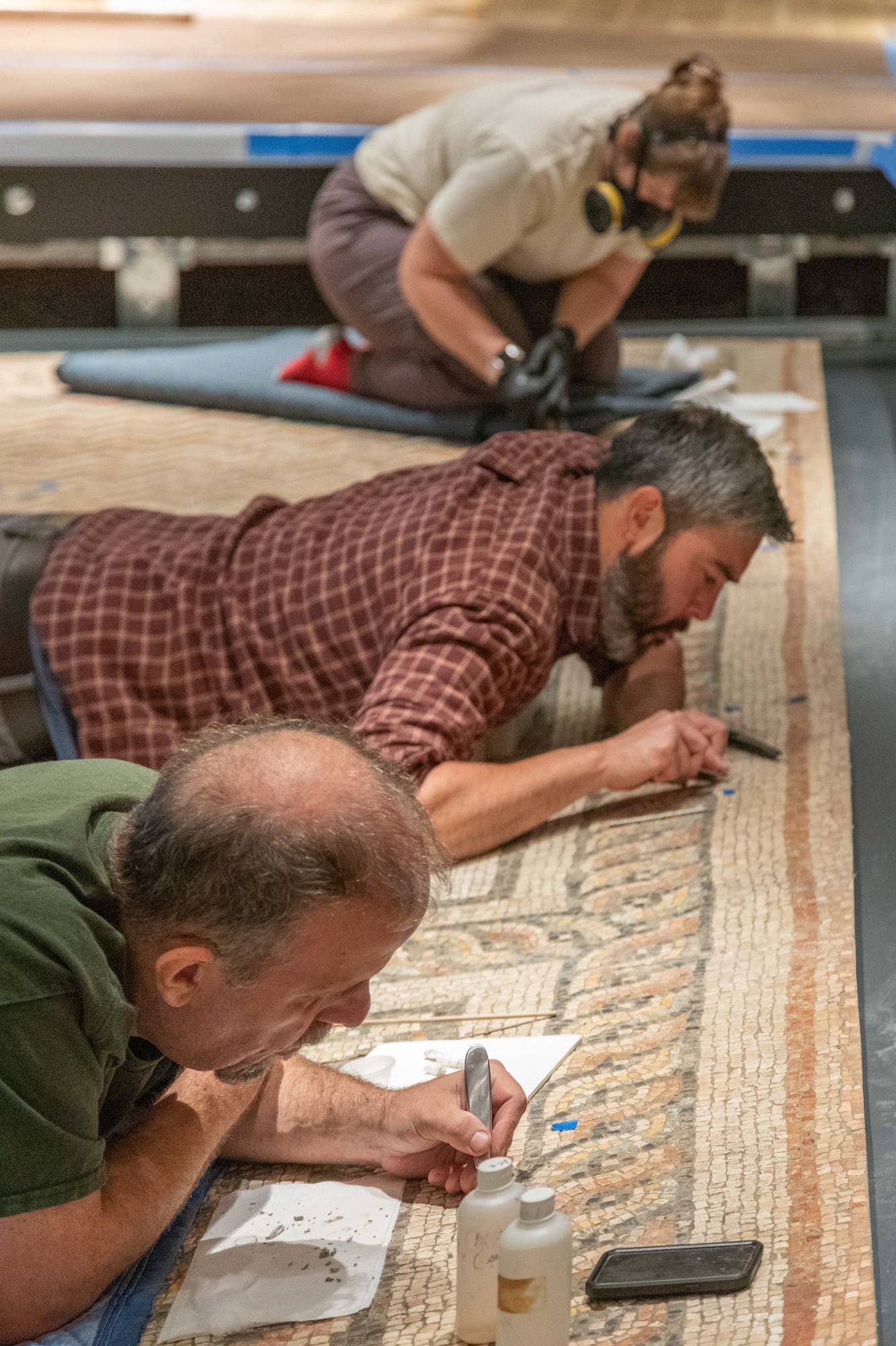 Working prone atop the mosaic, conservators make final touches on the installation.