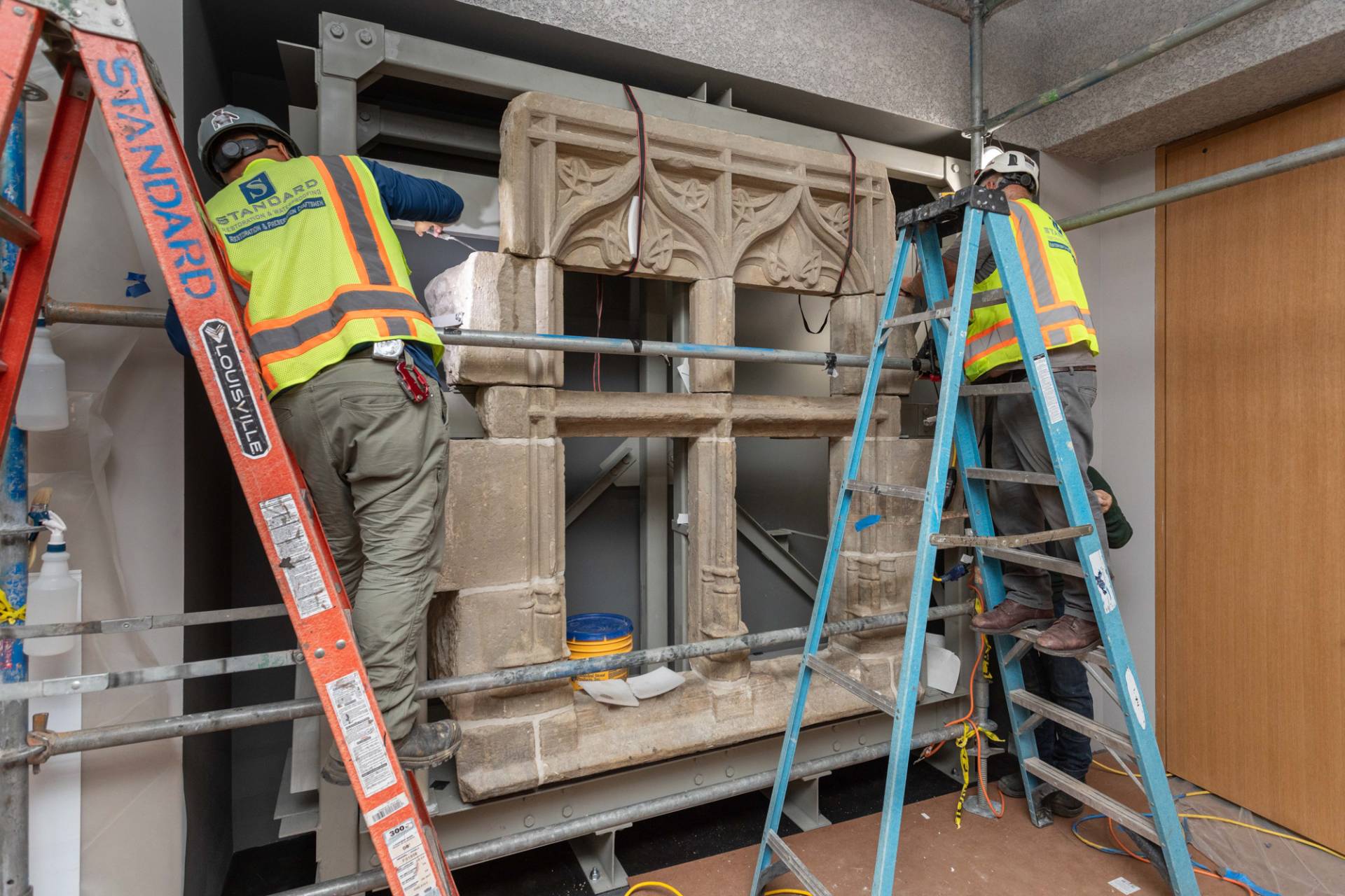 Workers on ladders install a 15th century stone window from France.