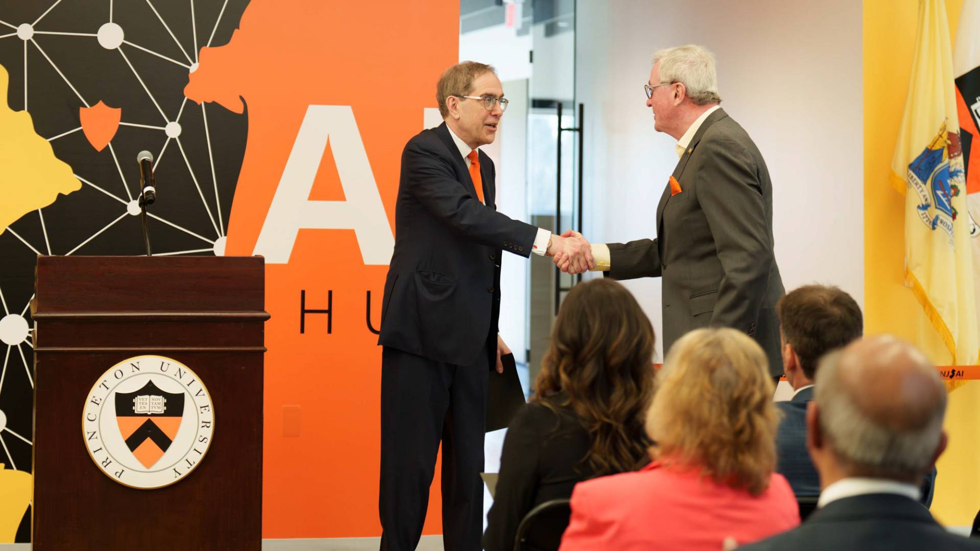 Chris Eisgruber and Phil Murphy shake hands in front of the NJ AI logo.